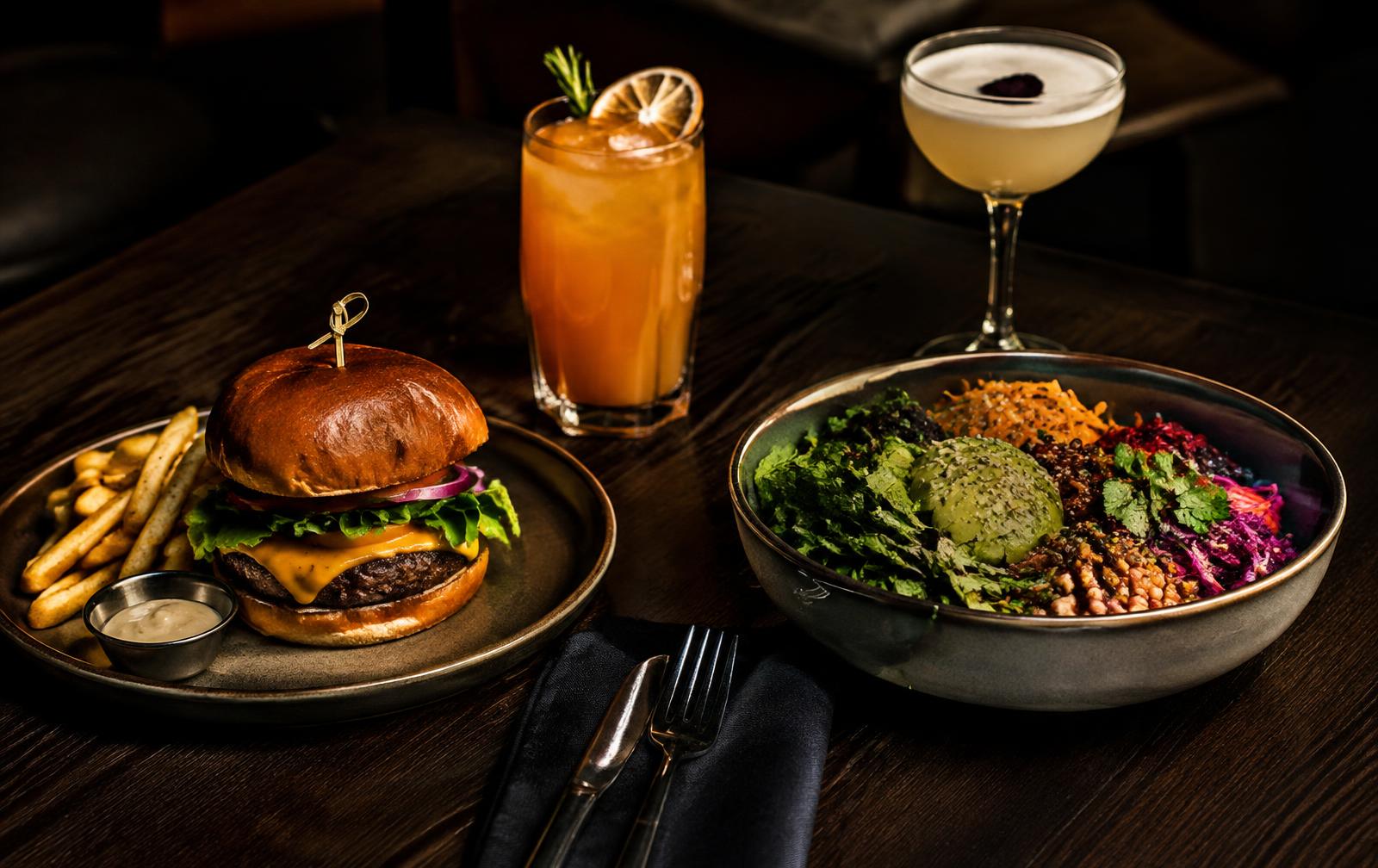 Burger, colorful bowl, and drinks on a dark table