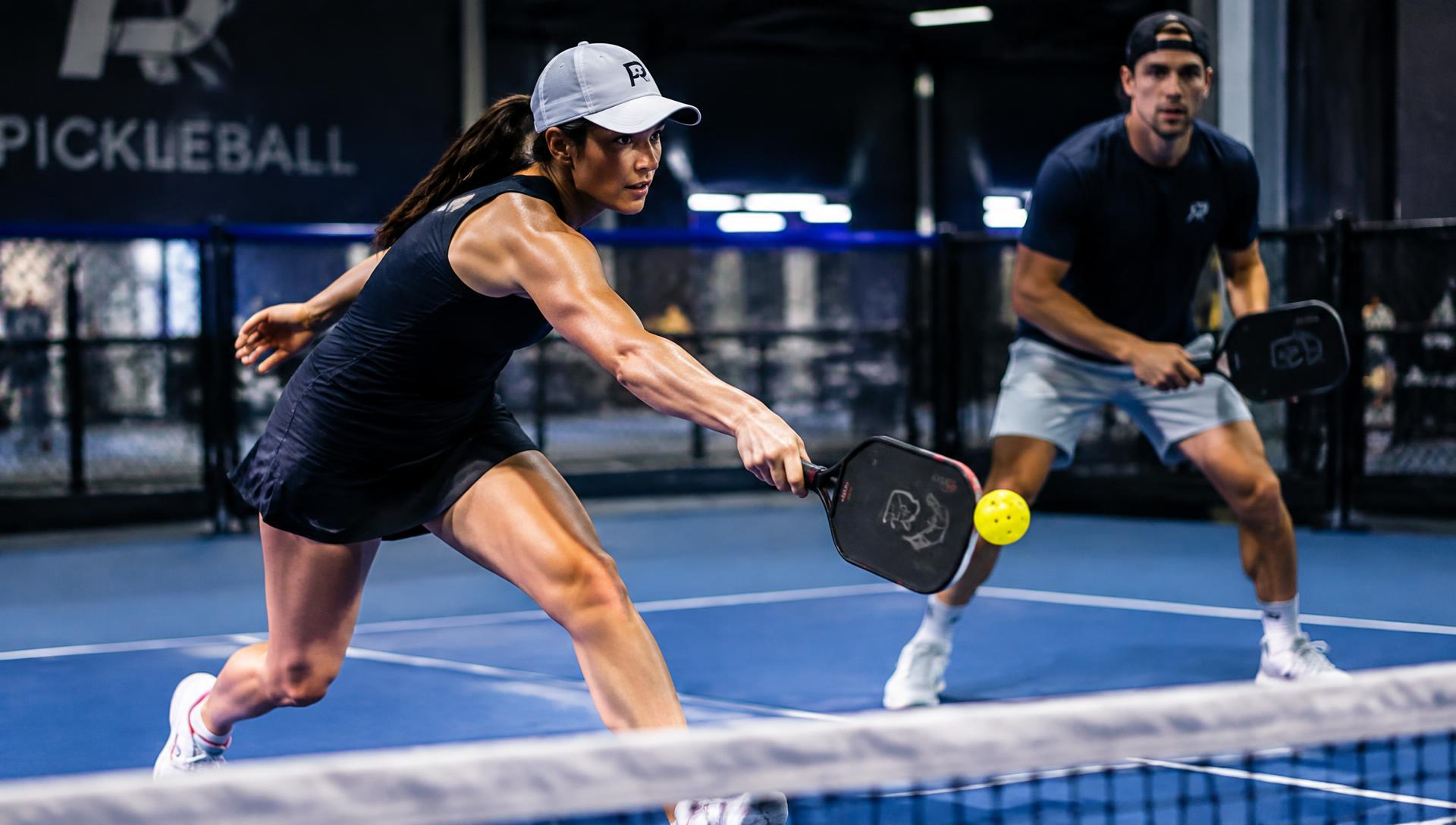 Two players in an intense indoor pickleball doubles rally